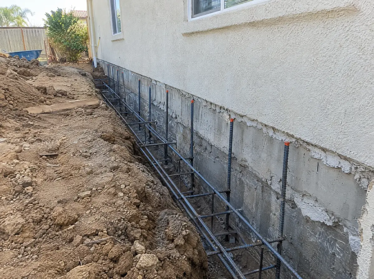 Footing trench along the back of a stucco house with rebar doweled into the existing foundation
