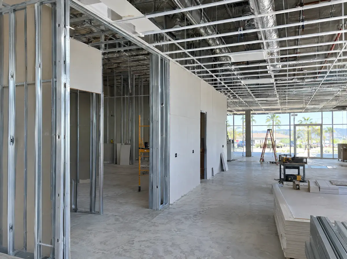 Inside a commercial tenant space with new metal stud walls, drywall partly hung and a ceiling grid going up