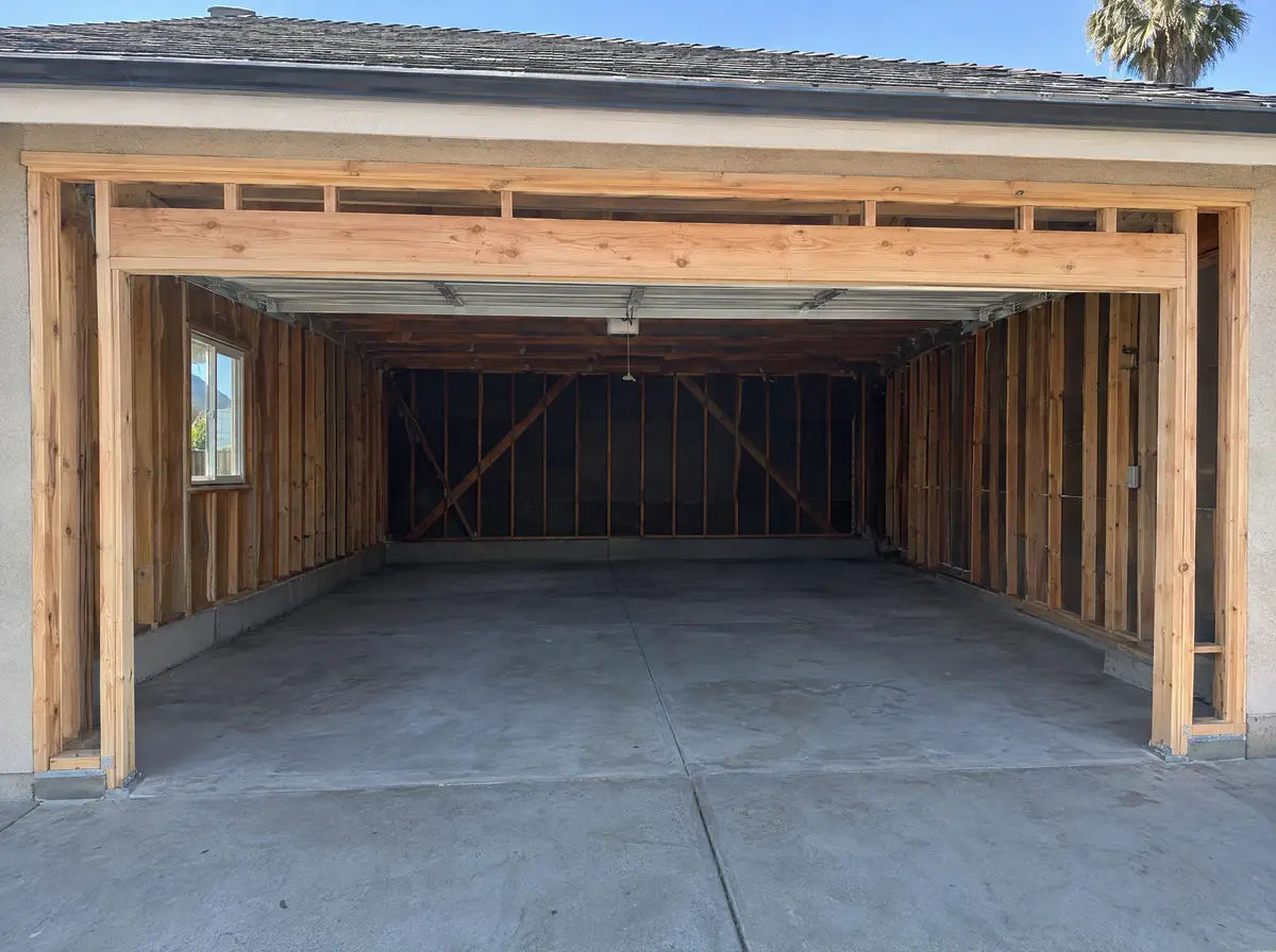 Inside an emptied two-car garage, the garage door opening framed in with new wood studs and a window header