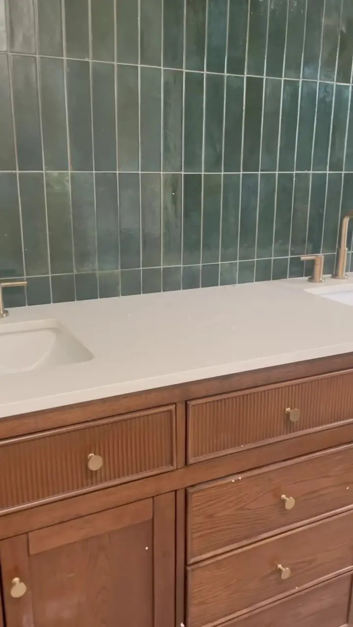 Double vanity with vertical green tile and brass faucets