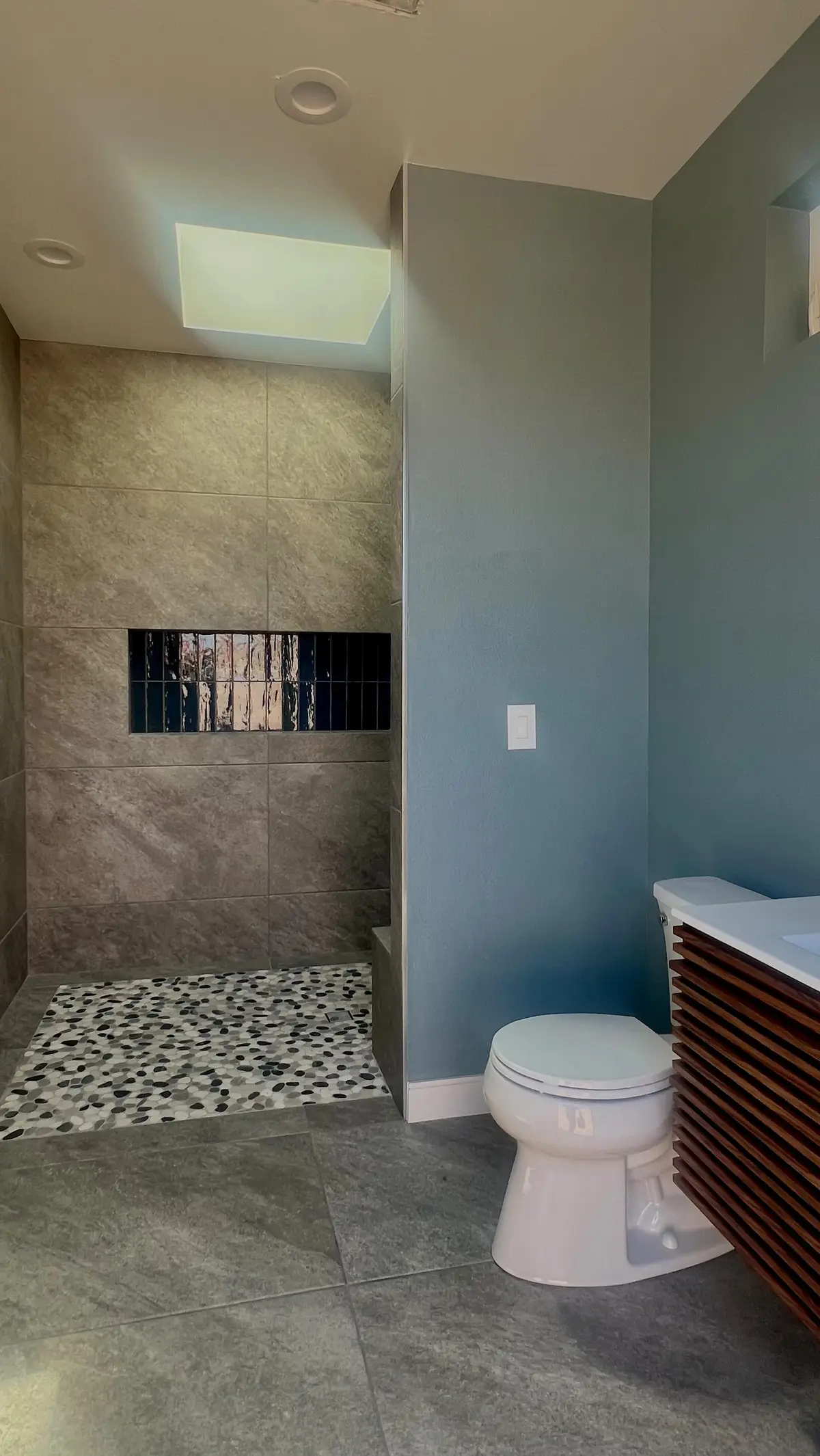 893 sq ft ADU and pool house, two phases in Fontana, CA: outdoor bathroom with pebble shower floor and wood slat vanity