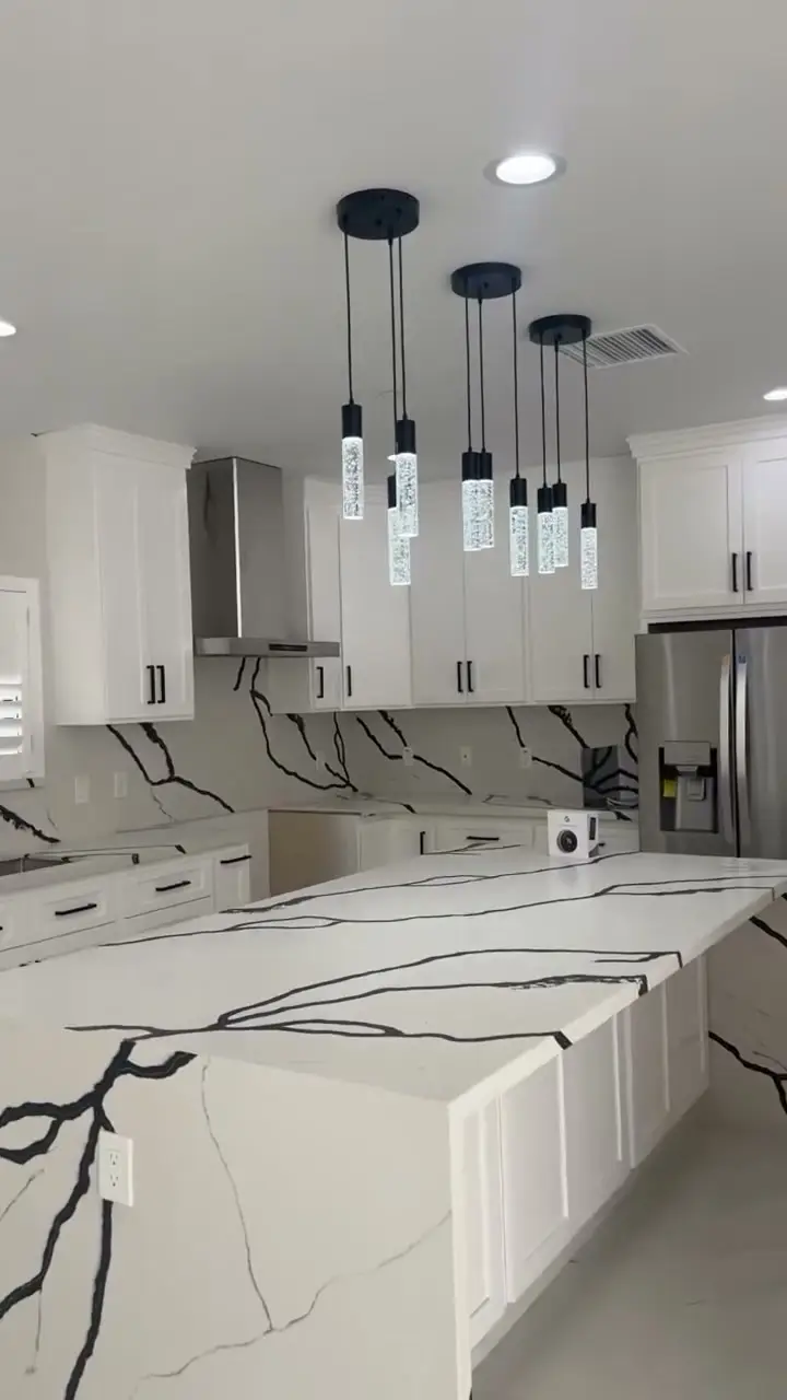 Custom home with a glass garage door in Whittier, CA: white kitchen with veined quartz counters and black pendant lights